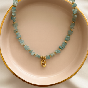 Necklace with turquoise beads and a gold charm on a pink plate