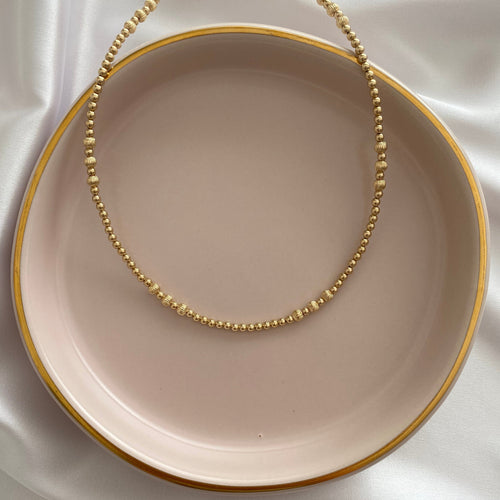 Necklace on a beige plate with a gold chain against a white fabric background