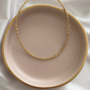 Necklace on a beige plate with a gold chain against a white fabric background