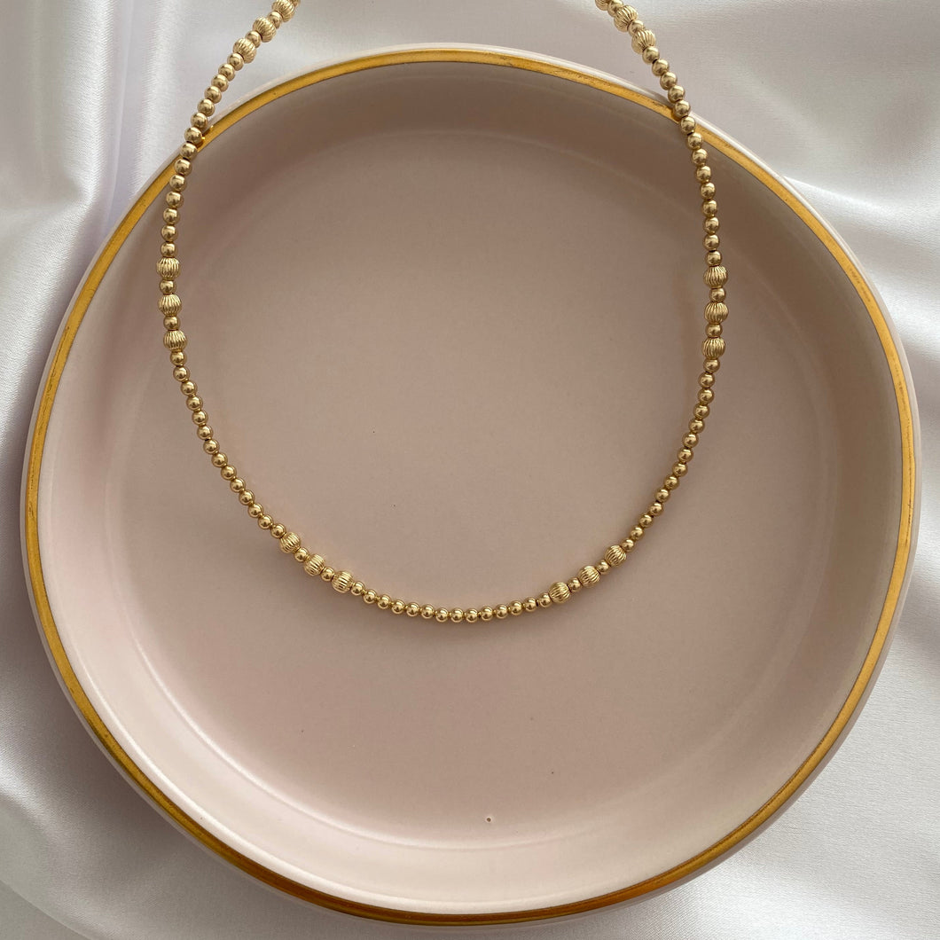 Necklace on a beige plate with a gold chain against a white fabric background